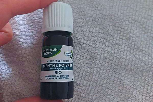 Une personne tenant entre ses doigts une huile essentielle à la menthe poivrée