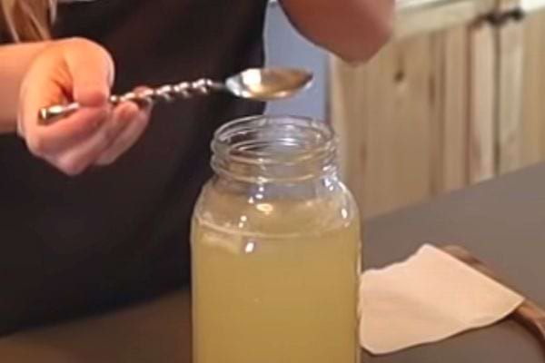 Une personne tenant une cuillère à soupe au dessus d'un pot rempli de vinaigre