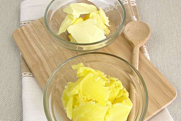 Du beurre dans deux coupelles en verre sur une planche à découper en bois avec une cuillère en bois