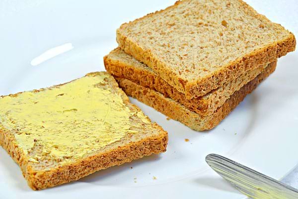 Du beurre sur une tranche de pain complet avec plusieurs tranches l'une sur l'autre avec un couteau