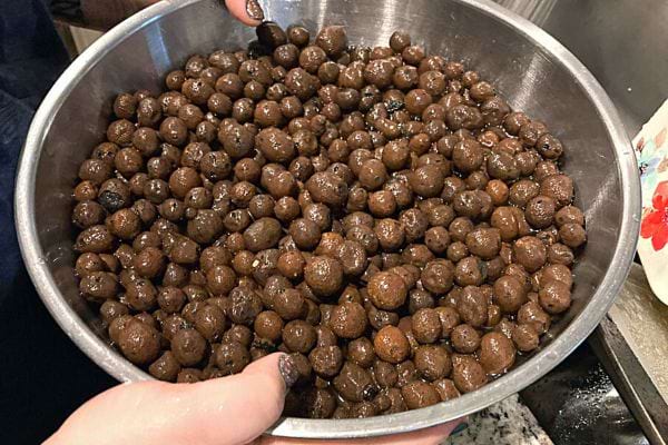 Une femme qui tient un bol en acier remplie de billes d'argiles