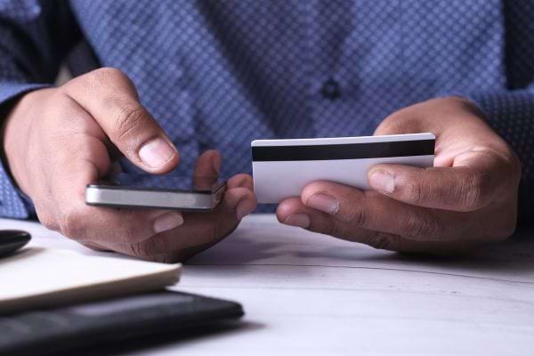 Un homme tenant un smartphone ainsi qu'une carte bancaire dans les deux mains 
