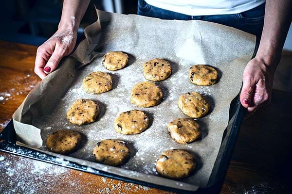 Une femme tenant une plaque de cuisson avec plusieurs cookies dessus 