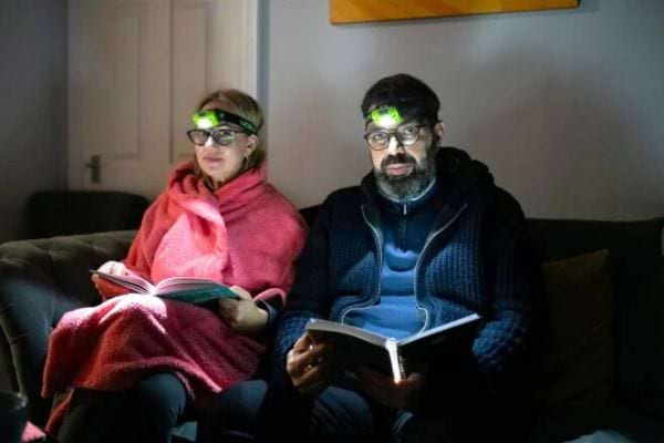 Un couple dans le noir qui tient un livre dans leurs mains avec une lampe sur leurs têtes 