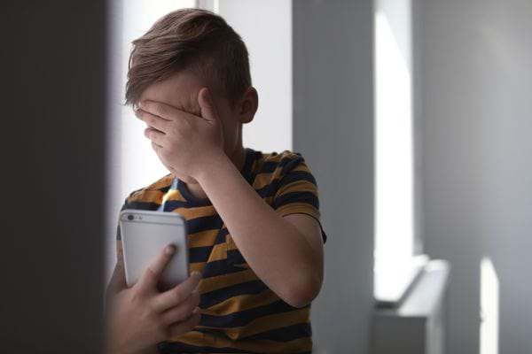 Un enfant qui se cache les yeux tenant un smartphone gris 