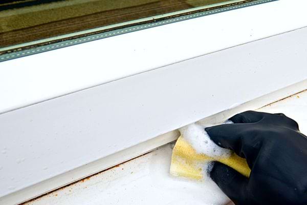 Une personne nettoyant une fenêtre avec une éponge jaune et de la mousse
