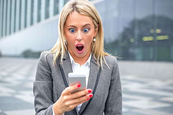 Une femme blonde sur son smartphone avec un air choqué 