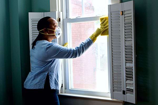Une femme noire avec un masque nettoyant une vitre