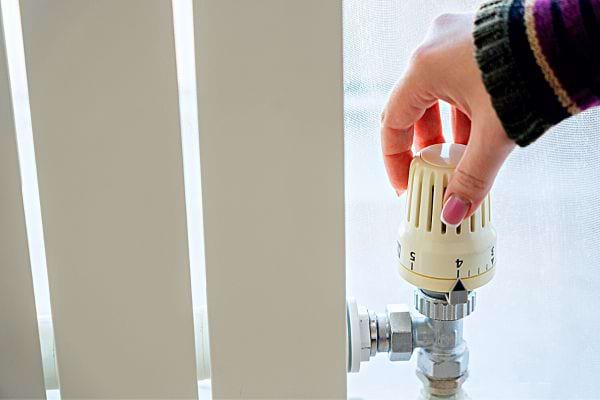 La main d'une femme avec des faux ongles rose réglant son radiateur