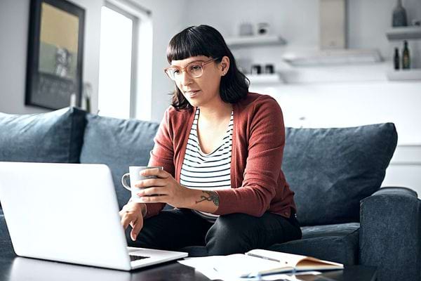 Une femme qui tient une tasse devant son pc 