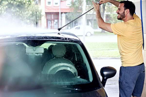 Un homme qui nettoie sa voiture avec un jet d'eau 
