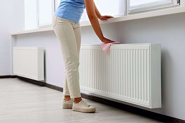Une femme nettoyant son radiateur à l'aide d'un chiffon rose