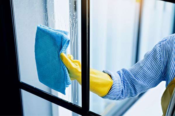 Une personne portant des gants jaunes en latex nettoyant une vitre avec un chiffon bleu