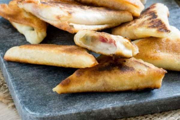 Des Samossas au gorgonzola, poire et jambon cru sur une planche en pierre 