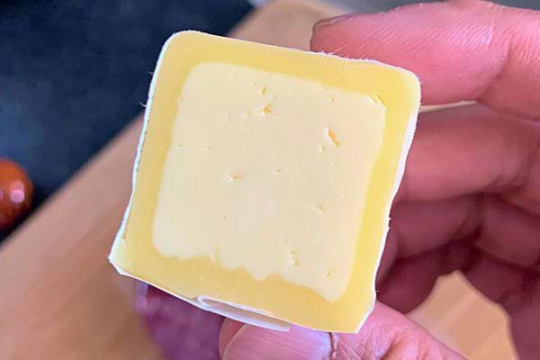 Une main tenant un carré de beurre, montrant sa texture crémeuse et sa couleur jaune pâle.