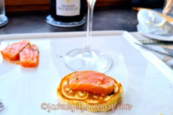 Blinis avec saumon mariné et zeste de citron sur une assiette blanche.