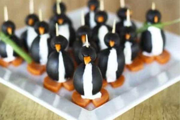 Brochettes créatives en forme de pingouins faites d'olives, de carottes et de fromage.
