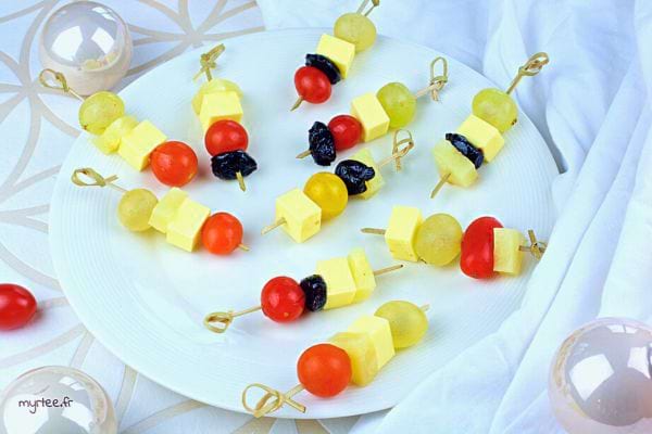 Brochettes de fromage jaune, tomates cerises, et fruits secs sur fond blanc.