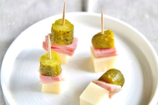 Brochettes de jambon, fromage et cornichons sur assiette blanche.