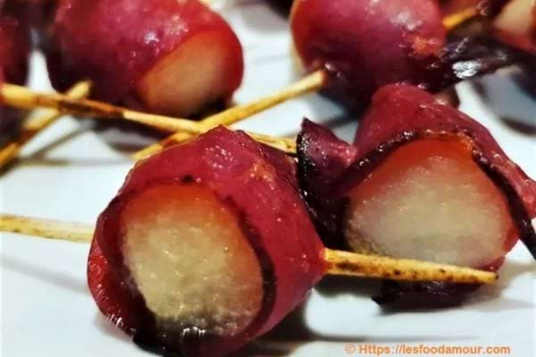 Brochettes de magret de canard enroulé autour de poires, présentées sur fond sombre.