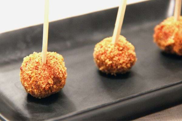 Boulettes de pain d'épices sur bâtonnets, disposées sur une assiette noire.