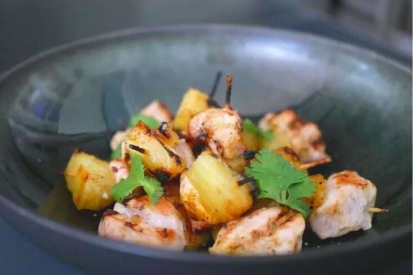 Brochettes de poulet et ananas grillés dans un bol en verre avec une touche de coriandre.