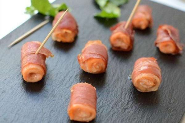 Roulés de saumon fumé et lard sur une ardoise noire.