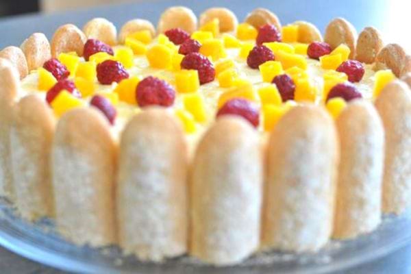 Charlotte exotique sans cuisson, entourée de biscuits à la cuillère, avec des morceaux de mangue et des framboises.