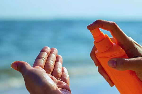 Mains appliquant de la crème solaire pour prévenir les rides du cou et du décolleté.