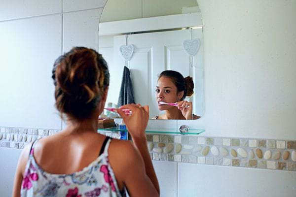 Une femme se brosse les dents devant le miroir de sa salle de bain.
