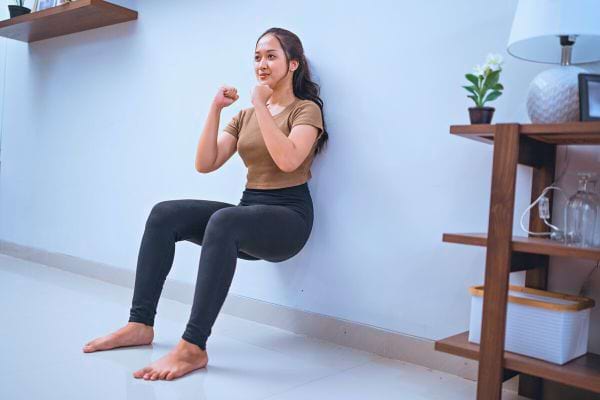 Femme réalisant l'exercice de la "chaise" contre un mur pour les cuisses.