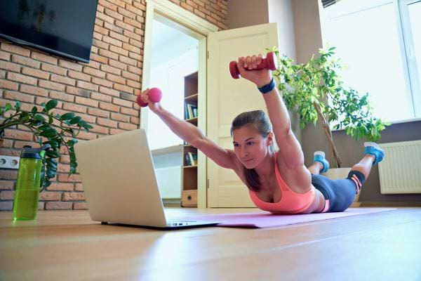 Femme exécutant l'exercice "Superman" avec haltères pour cibler le dos et les épaules.