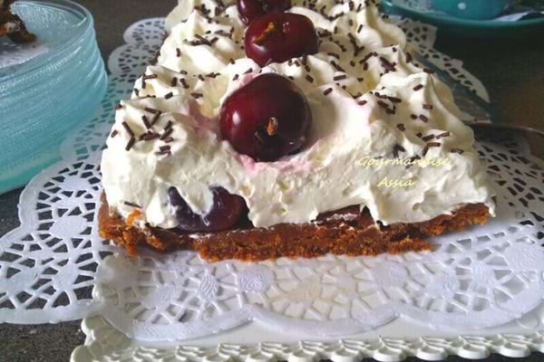 Forêt noire sans cuisson avec des cerises et une garniture à la crème fouettée, présentée sur un napperon.