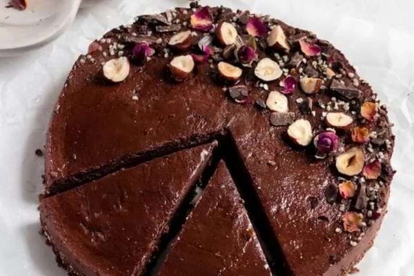 Gâteau vegan sans cuisson, parsemé de noisettes, pétales de roses et éclats de cacao.