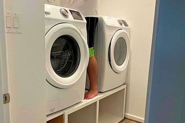 Pieds d'une personne émergeant d'une machine à laver dans une salle de bain blanche.