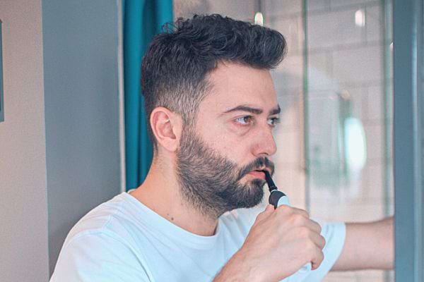Un homme se brosse les dents attentivement devant un miroir.