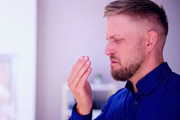Un homme vérifie son haleine, main devant la bouche, expression préoccupée.