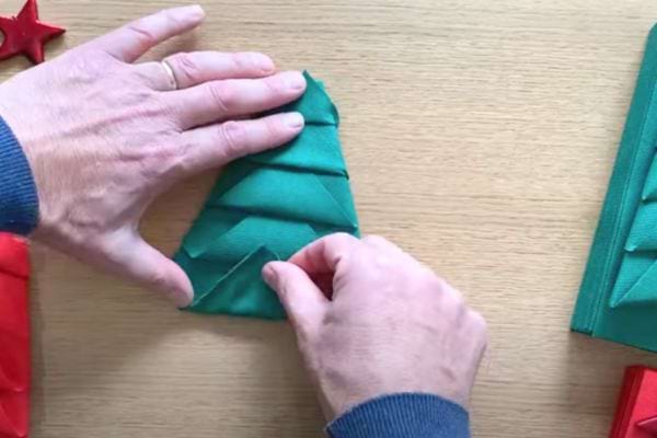 Les plis de la serviette forment un sapin, une main ajuste le dernier pli.