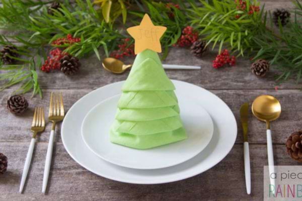 La serviette verte est pliée en forme de sapin de Noël sur une assiette blanche.