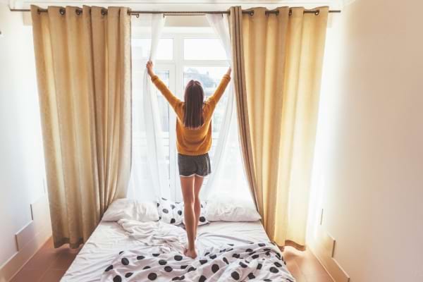 Une femme qui ouvre les rideaux le matin pour aérer son lit