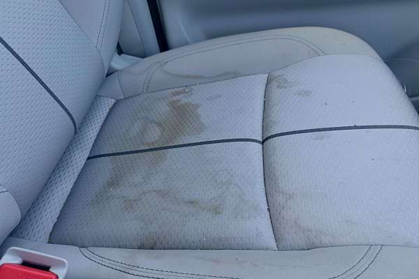 Des éclaboussures et taches de café sur un siège de voiture en tissu clair.