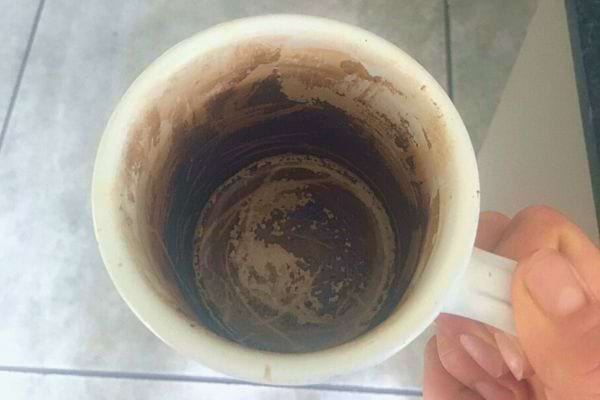 Résidus de marc de café au fond d'une tasse blanche tenue par une main.