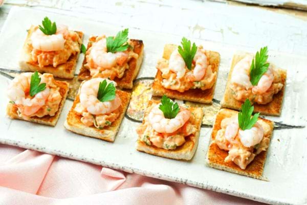 Toasts carrés avec crevettes roses et sauce crémeuse garnis de persil.