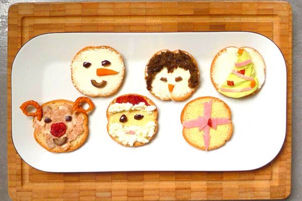 Assortiment de toasts pour enfants avec des visages de personnages de Noël faits de divers ingrédients.