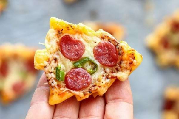 Petites pizzas en forme d'étoiles décorées comme des sapins de Noël avec des garnitures colorées.