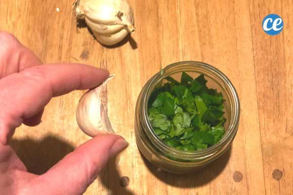 Persil haché placé dans un petit bocal en verre à côté d'une gousse d'ail.