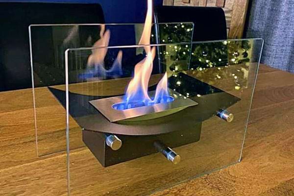 Foyer bioéthanol portable entouré de verre sur une table en bois.