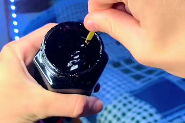 Spatule en bois en train de remuer un pot de Shilajit ouvert sur une table en bois.