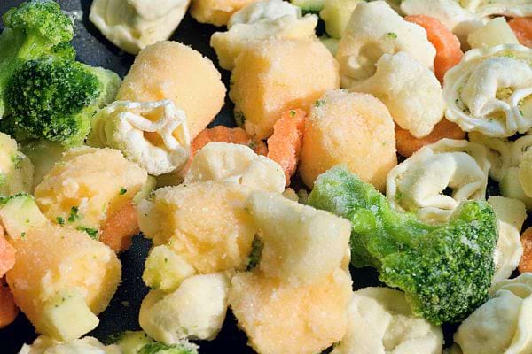 Assortiment de légumes surgelés, dont des tortellini, du brocoli, et des carottes, recouverts de glace.
