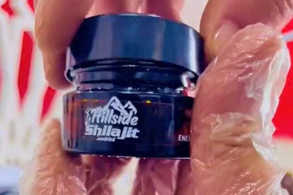 Main en gants ouvrant un pot de "Hillside Shilajit" scellé.